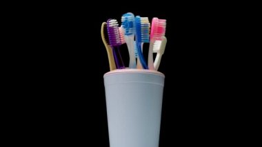Bardaktaki birçok diş fırçası siyah arka planda döner. Diş bakımı, çok renkli diş fırçaları. Pikapta diş fırçaları