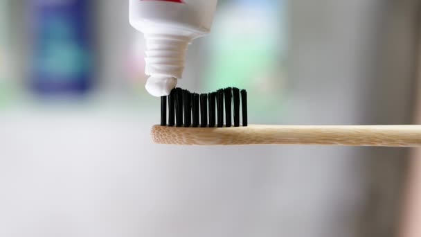 歯磨き粉は木製のエコ歯ブラシに適用されます 浴室のボケの背景をクローズアップしました 歯の洗浄コンセプト チューブから歯磨き粉を絞り出す — ストック動画