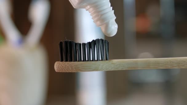特写牙膏适用于木制生态牙刷 在浴室的Bokeh背景上的特写 牙齿清洁的概念 把牙膏从管子里挤出来 — 图库视频影像