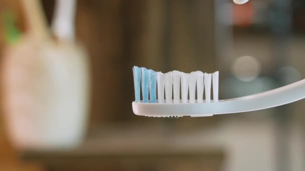 閉じる歯磨き粉は白い歯ブラシに適用されます 浴室のボケの背景をクローズアップしました 歯の洗浄コンセプト チューブから歯磨き粉を絞り出す — ストック動画