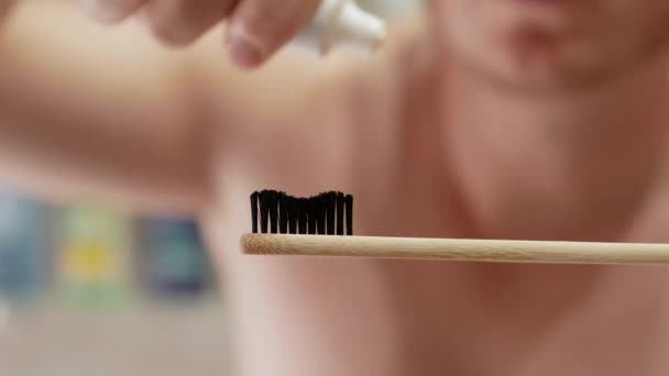 一个年轻人在浴室的牙刷上挤牙膏 一个手里拿着牙膏的男人 — 图库视频影像