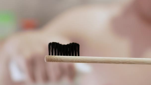 モデル生意気な笑顔の青年がバスルームの歯ブラシに歯磨き粉を絞る 歯磨き粉のチューブを手にした男 白い歯を磨くというコンセプト — ストック動画