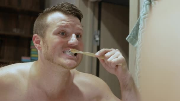 鏡の前の浴室でハンサムな若い男が歯を磨く 歯磨き粉のチューブを手にした男 白い歯を磨くというコンセプト — ストック動画