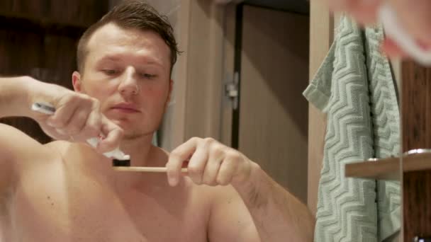 バスルームで歯を磨くハンサムな若い男 歯磨き粉のチューブを手にした男 白い歯を磨くというコンセプト — ストック動画