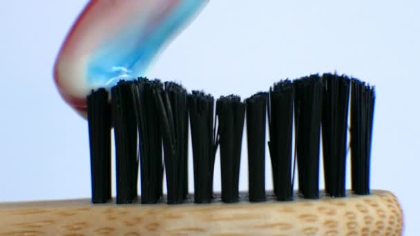白い背景に木製の歯ブラシにマルチカラーの歯磨き粉を絞る 白い歯のコンセプト — ストック動画