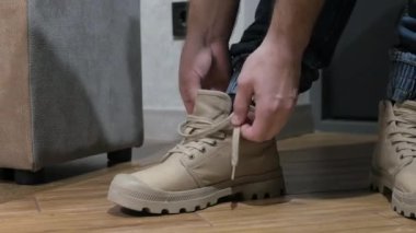 Genç bir adam bacağına ayakkabı giyer, erkek gri ayakkabıları giyer. Adamın elleri ayakkabıları bağlıyor. Erkek çizmeleri.