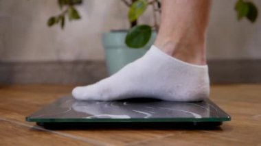 Bir adam zemin terazisine çıkar, kilo verme konsepti, beyaz çoraplı adamların bacaklarının yakın çekimi terazide durur.