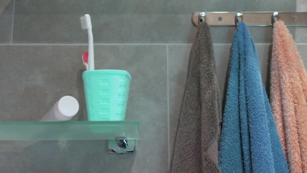 バスルームの白いバスケットに歯ブラシの動きのアニメーションを停止します 健康的な歯の概念 浴室のガラス棚のカラフルな歯ブラシ クロムハンガーのシャワーのタオル — ストック動画