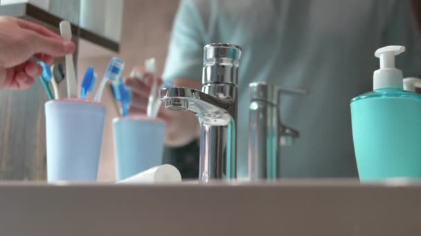 スローモーション男はバスルームの鏡の前の水道水の下で歯ブラシを洗う 歯のケア 健康な歯の概念 男はバスルームで歯を磨く — ストック動画