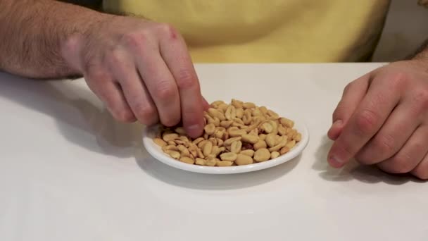 塩辛いピーナッツを食べる 男の手はピーナッツのマメ科植物を食べる 若い男はナッツを食べることでエネルギーを補充します — ストック動画
