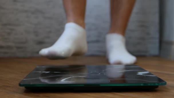 白い靴下の男性の足は床の鱗に立っている 人は体重をコントロールするために体重計で量られます 減量の概念 体重計の男の体 — ストック動画