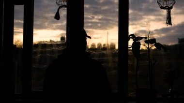 Depresyondaki adam patlama dalgasından korunmak için arka plandaki mühürlü pencerelere karşı, pencereden gökyüzüne bakarak, evde savaştan saklanan bir adam. Depresyondaki bir adam füze saldırısından kaçıyor. Ülkede sıkıyönetim döneminde bir adam.