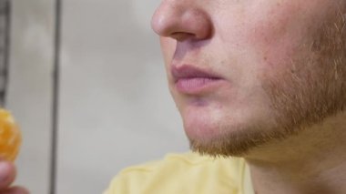Yakın plan adam sağlıklı meyve mandalinasının tadını çıkarıyor. Genç ve yakışıklı bir adam C vitamini ile çin meyvesi dilimleri yer.