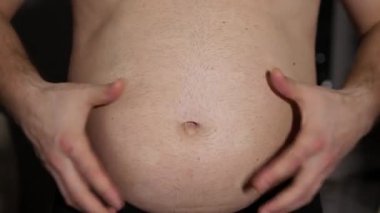 Şişman bir adam büyük bir göbek gösterir. Şişmiş bira göbeği olan bir adam. Vücut ağırlığıyla ilgili sorunlar. Genç bir adamın obezitesi