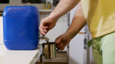 Evde bir kişi yedek bir kaynaktan içme suyu topluyor. Teneke kutudan bardağa su dök. Su sıkıntısı çekiyor. Bir adam musluğu su dolu bir kutuda sökerek su topluyor. Evde musluk suyu yok.