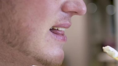 Yakın çekim, gülümseyen genç adam cips yiyor, sağlıksız yemek yiyor. Pembe kapüşonlu bir adam kızarmış patates yer ve çiğner. Fast food
