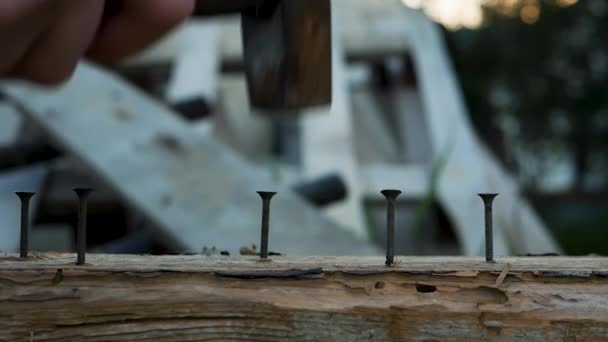 手すりのハンマーがハンマーで木の塊に釘を打ち込む ハンマーで釘を2本 木造建築物を造る男 — ストック動画