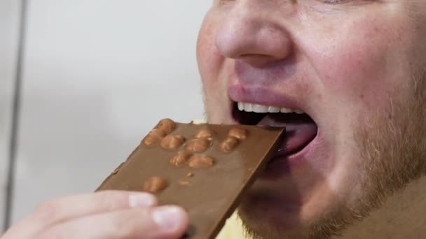 美しい笑顔の男がナッツとチョコレートを食欲をそそる食べます 男はミルクチョコレートを食べの肖像画クローズアップ チョコレートを歯で噛んだ男 — ストック動画