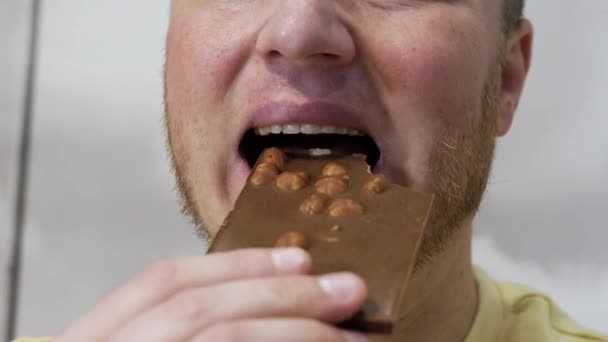 一个面带笑容的男人用坚果吃开胃的天然巧克力 一个近距离吃牛奶巧克力的男人的肖像 男人用牙齿咬着一块巧克力 — 图库视频影像