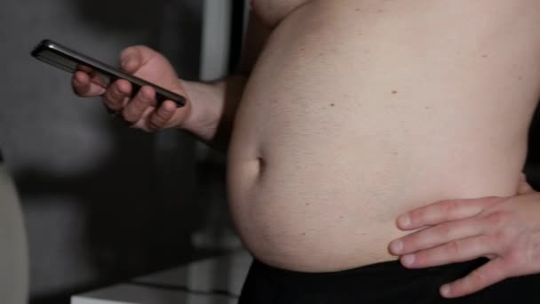 一个超重的男人表现出一个大肚子 那个人正在用电话打字 体重的问题 一个年轻人的肥胖问题 — 图库视频影像