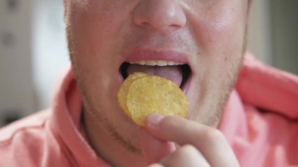 閉じるまでのスローモーション笑顔若い男は 不健康な食品チップを食べている 男はポテトを食べて噛んだ — ストック動画