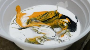 Yakın plan akrilik boyaları bir kaptaki spatulayla karıştırmak. İç mekânda resim yapmak. Sanatçı, duvardaki resim için siyah ve sarı boyayı karıştırır. Yaratıcı resim
