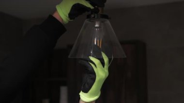 Özel iş eldivenli bir adam modern tavan lambasının yanında bir lambayı beceriyor. Yanmış bir ampulü sökmek, ampulü yavaş çekimde bir elektrikçiyle değiştirmek. İçeride elektrik tasarrufu kavramı