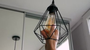 Yaşlı bir adamın eli yenisinin yerine modern bir tavan lambasının vidasını söker. Yanmış ampulü sök, ampulleri yavaş çekimde elektrikçiyle değiştir. İçeride elektrik tasarrufu kavramı.