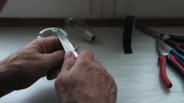 Elektrikçi teli bıçakla söktü. Elektriği kabloya bağlıyorum. Bir adam bir lambayı bağlamak için kabloyu keskinleştirir.