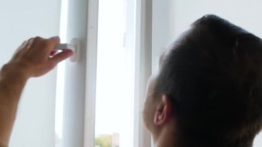 Evde ısı tasarrufu kavramı, insan ısıdan tasarruf etmek için plastik pencereleri kapatır. Genç adam dairedeki pencereyi kapattı.