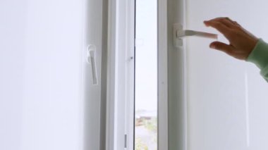 Evde ısıyı kurtarma kavramı, sıcak ceketli bir adam yavaş çekimde ısıdan tasarruf etmek için evdeki bütün plastik pencereleri kapatır. Genç adam dairedeki pencereyi kapattı. Beyaz plastik pencere