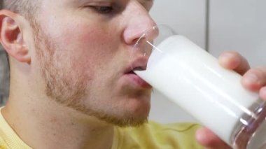 Şeffaf bardaktan taze süt içen bir adamın yakın çekimi. Kefir ya da süt ürünü içen bir adamın portresi