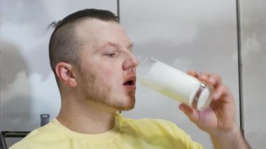 Genç yakışıklı bir adam iştah açıcı bir şekilde taze süt ya da şeffaf bir bardaktan milkshake içer. Kefir ya da süt ürünü içen bir adamın portresi. Vücuttaki kalsiyum kaynağını bir ürünle doldurmak.