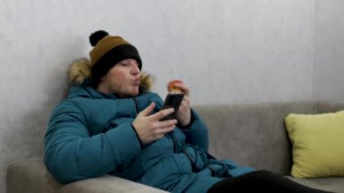 Bir adam evde soğuktan donarak elma yer ve telefonuna benzin krizi mesajları yazar. Bir adam kanepede otururken akıllı telefonda bir şeyler yazıyor. Evde ceketli ve şapkalı bir adam var..