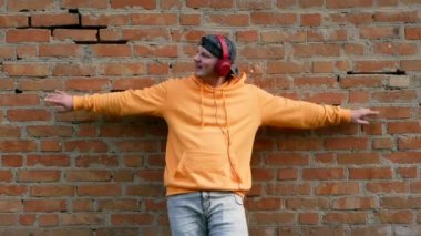 Kulaklıklı, dans ederken müzik dinleyen kapüşonlu genç adam. Tuğla duvar arkasında kulaklıklı şık bir adam portresi.