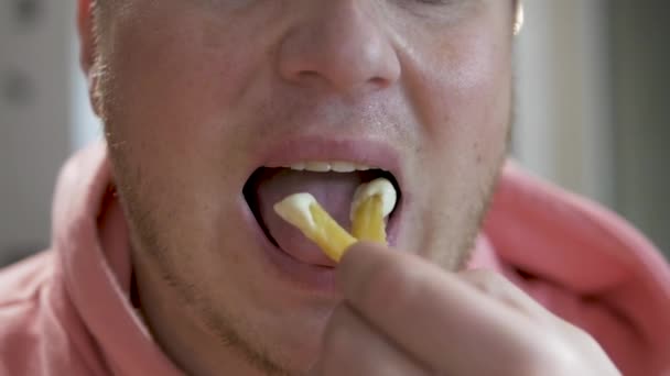 慢动作的年轻人吃着带有酱汁的薯条和不健康的食物 一个穿着粉色帽衫的男人吃着炸土豆 然后咀嚼它 快餐店里的快餐 — 图库视频影像