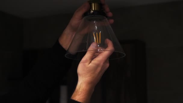 一个男人在一个现代的天花板灯旁边拧着灯 拧开烧坏的灯泡 用电工慢动作更换灯泡 室内节电的概念 — 图库视频影像