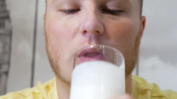 透明なガラスから新鮮な牛乳をおいしく飲んでいる男のクローズアップ 男がケフィアや乳製品を飲んでいる肖像画 体内のカルシウム埋蔵量を補充する — ストック動画