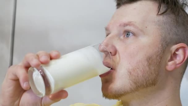 透明なガラスから新鮮な牛乳をおいしそうに飲む青年 男がケフィアや乳製品を飲んでいる肖像画 乳製品で体内のカルシウムの供給を補充する — ストック動画
