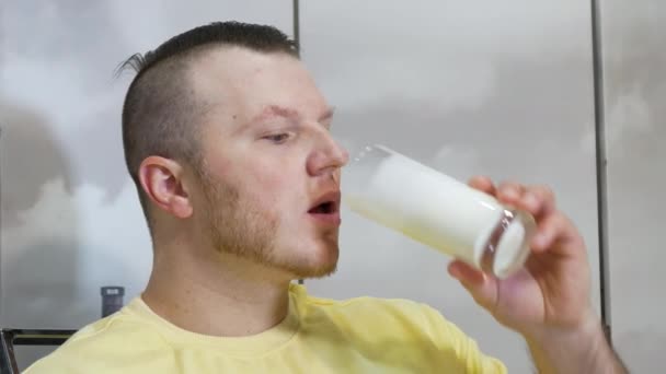 若いハンサムな男が食欲をそそり 透明なガラスから新鮮な牛乳やミルクシェイクを飲む 男がケフィアや乳製品を飲んでいる肖像画 製品で体内のカルシウムの供給を補充する — ストック動画