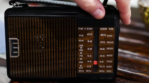 特写一个人在一张旧木桌上为收音机的无线电波调音 带有天线的古董接收机 按比例调模拟收音机 一个人在旧收音机里听新闻 听音乐 — 图库视频影像