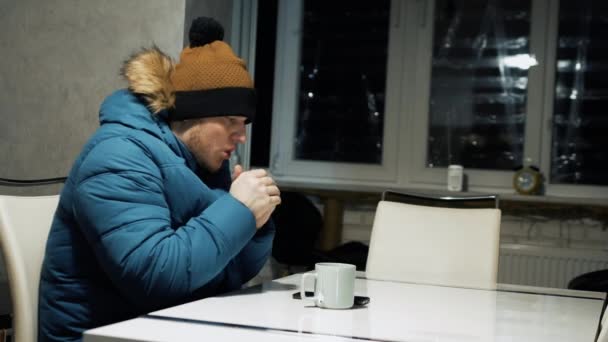 房子里供热不足 家里一个穿着夹克和帽子的人因寒冷而冻僵了 一个人在乌克兰的战争中沐浴 一个人用热茶取暖 房屋内的热电通讯受到损害 — 图库视频影像
