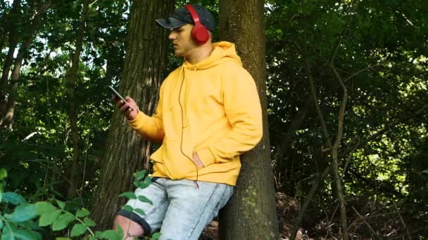 Який Фокус Сумний Молодий Чоловік Слухає Музику Навушниках Сидячи Лісі — стокове відео