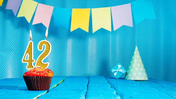Happy birthday card with a muffin decorated with a festive cake and burning candles. Copy space. Beautiful background happy birthday on the background of blue boards with a number of candles number 42.