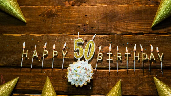 Top view of the golden letters of the candle with the number happy birthday, the background of the pie with candles happy birthday on the background of brown stranded boards. Postcard Happy birthday  50