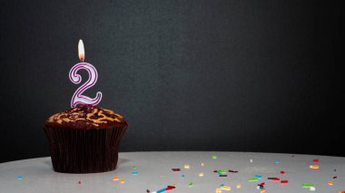 Siyah üzerine muffin ve 2 numaralı mumdan bir numara. Kopyalama alanı, siyah arkaplanda bir turta, doğum gününü kutlamak için bir kart, yıldönümü