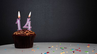 Siyah üzerine muffin, 14 numaralı mumdan bir numara. Kopyalama alanı, siyah arkaplanda bir turta, doğum gününü kutlamak için bir kart, yıldönümü