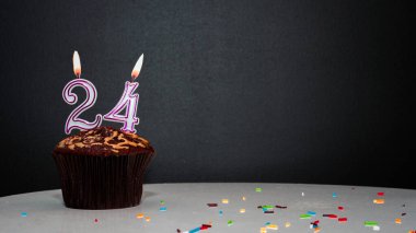 Siyah üzerine muffin ve 24 numaralı mumdan bir numara. Kopyalama alanı, siyah arkaplanda bir turta, doğum gününü kutlamak için bir kart, yıldönümü