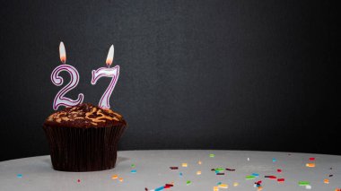 Siyah üzerine muffin, 27 numaralı mumdan bir numara. Kopyalama alanı, siyah arkaplanda bir turta, doğum gününü kutlamak için bir kart, yıldönümü