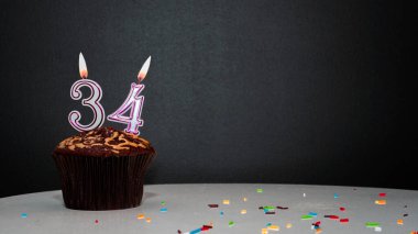Siyah üzerine muffin ve 34 numaralı mumdan bir numara. Kopyalama alanı, siyah arkaplanda bir turta, doğum gününü kutlamak için bir kart, yıldönümü